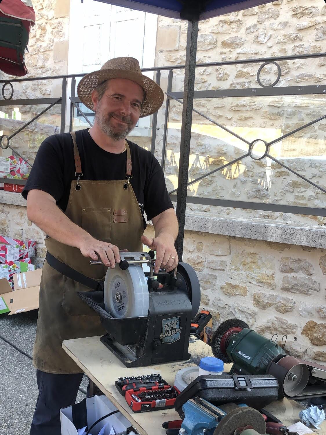 Fabien Azzalin, artisan affûteur, sur un marché derrière sa meule